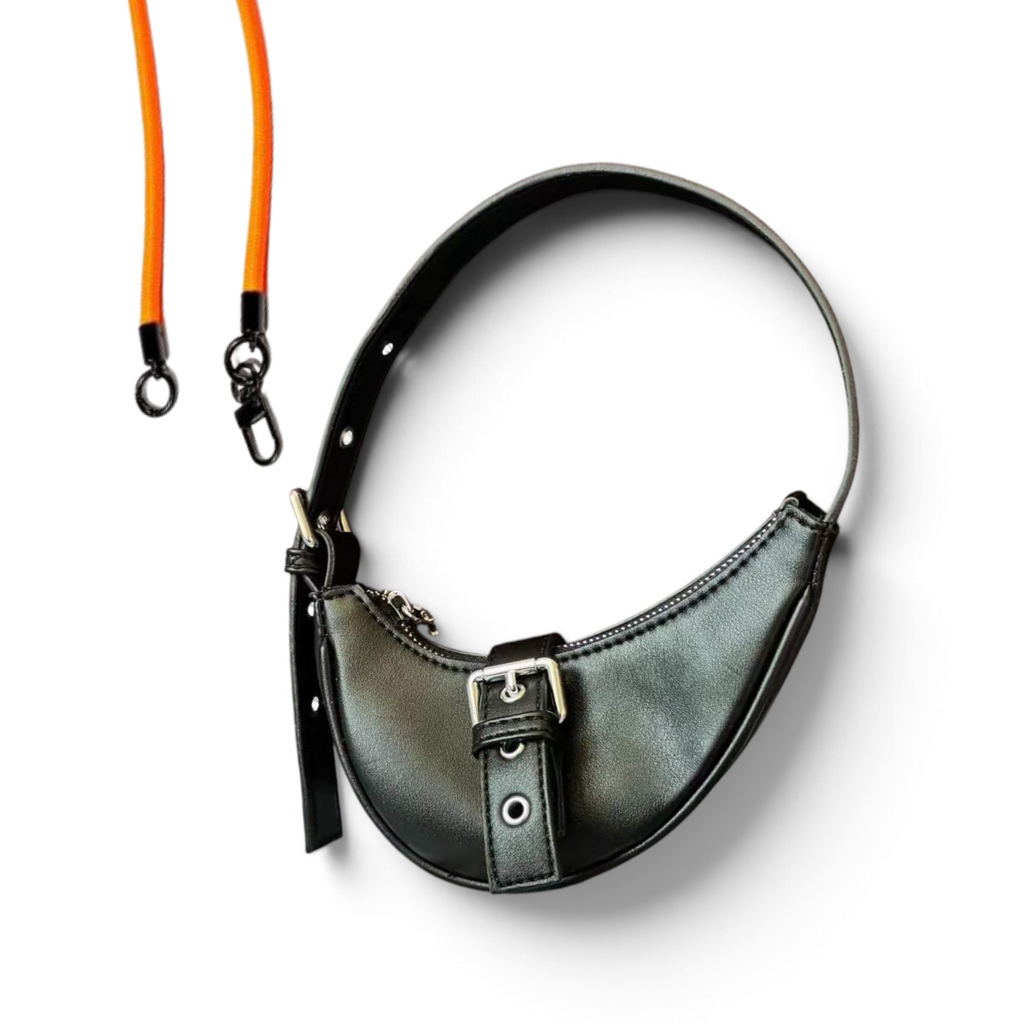 A crescent-shaped black leather shoulder bag with a buckle strap detail, shown on a white background with an orange detachable shoulder strap.