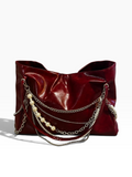 A glossy deep red leather shoulder bag featuring layered silver chains and a strand of white faux pearls draped over the front, set against a plain white background.