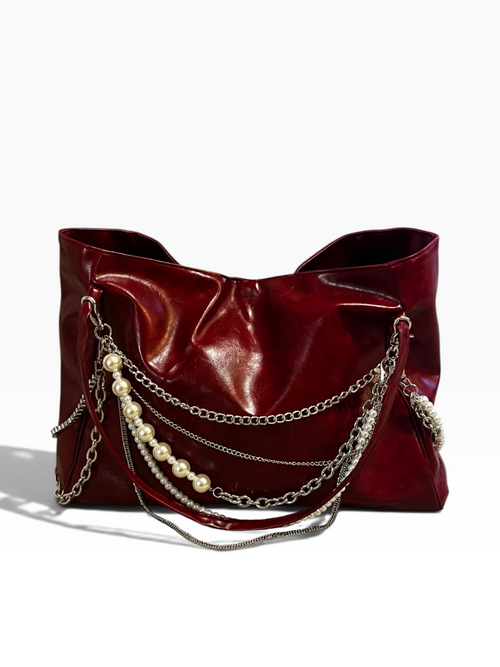 A glossy deep red leather shoulder bag featuring layered silver chains and a strand of white faux pearls draped over the front, set against a plain white background.