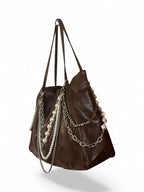 A dark brown leather shoulder bag decorated with silver chains and strands of white faux pearls, shown against a plain white background.