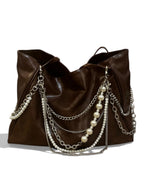 A dark brown slouchy leather shoulder bag decorated with draped silver chains and strands of white faux pearls, shown against a plain white background.