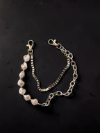 A silver-toned chain bracelet featuring a section of irregular white baroque pearls and lobster clasp ends, displayed on a dark textured background.