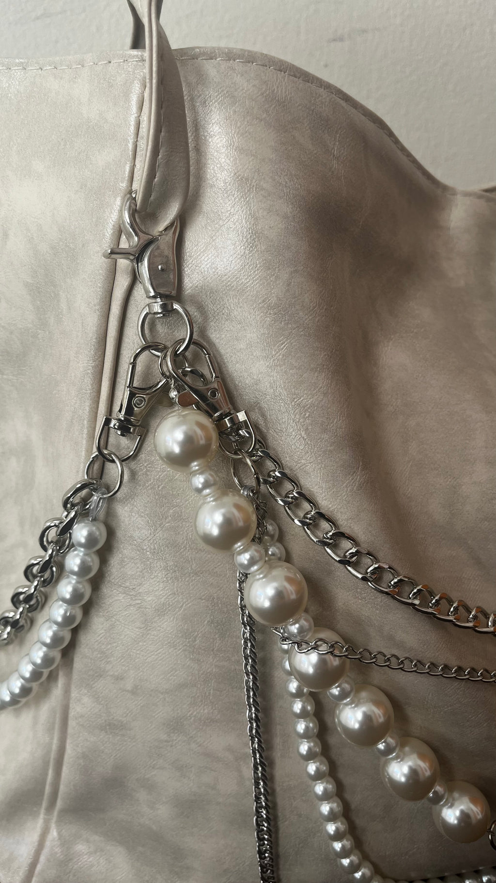 Close-up of a light beige leather shoulder bag featuring silver-tone chain straps adorned with white faux-pearl beads.