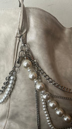 Close-up of a light beige leather shoulder bag featuring silver-tone chain straps adorned with white faux-pearl beads.