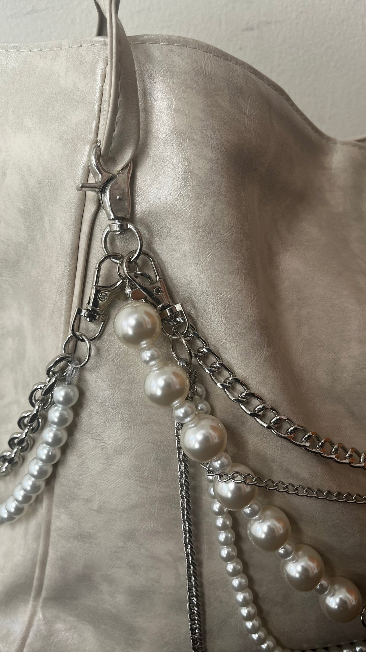 Close-up of a light beige leather shoulder bag featuring silver-tone chain straps adorned with white faux-pearl beads.