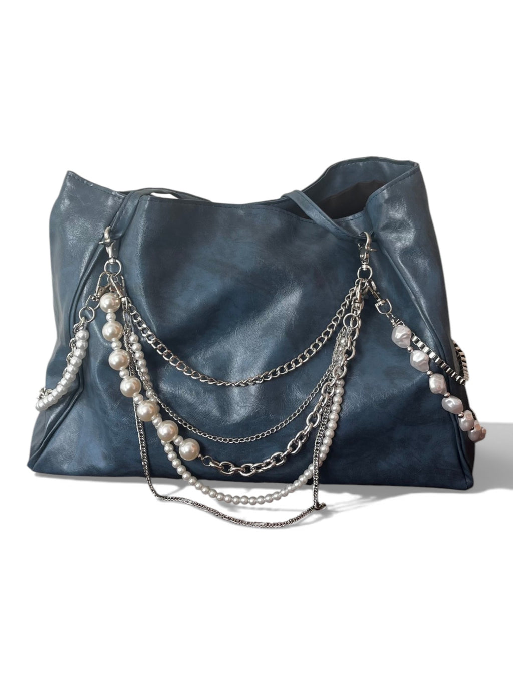A dark blue leather hobo bag featuring layered silver chains and pearl strands draped over the front, set against a plain white background.