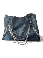 A dark blue leather hobo bag featuring layered silver chains and pearl strands draped over the front, set against a plain white background.