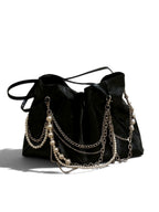 A black leather slouchy shoulder bag decorated with multiple draped silver chains and strands of white faux pearls, shown on a plain white background.